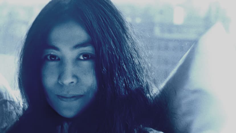 Close-up portrait of Yoko Ono with long dark hair, photographed through a car window in cool blue tones.