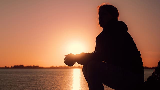 Woman as a silhouette reflecting and looking out to a view of the sunset