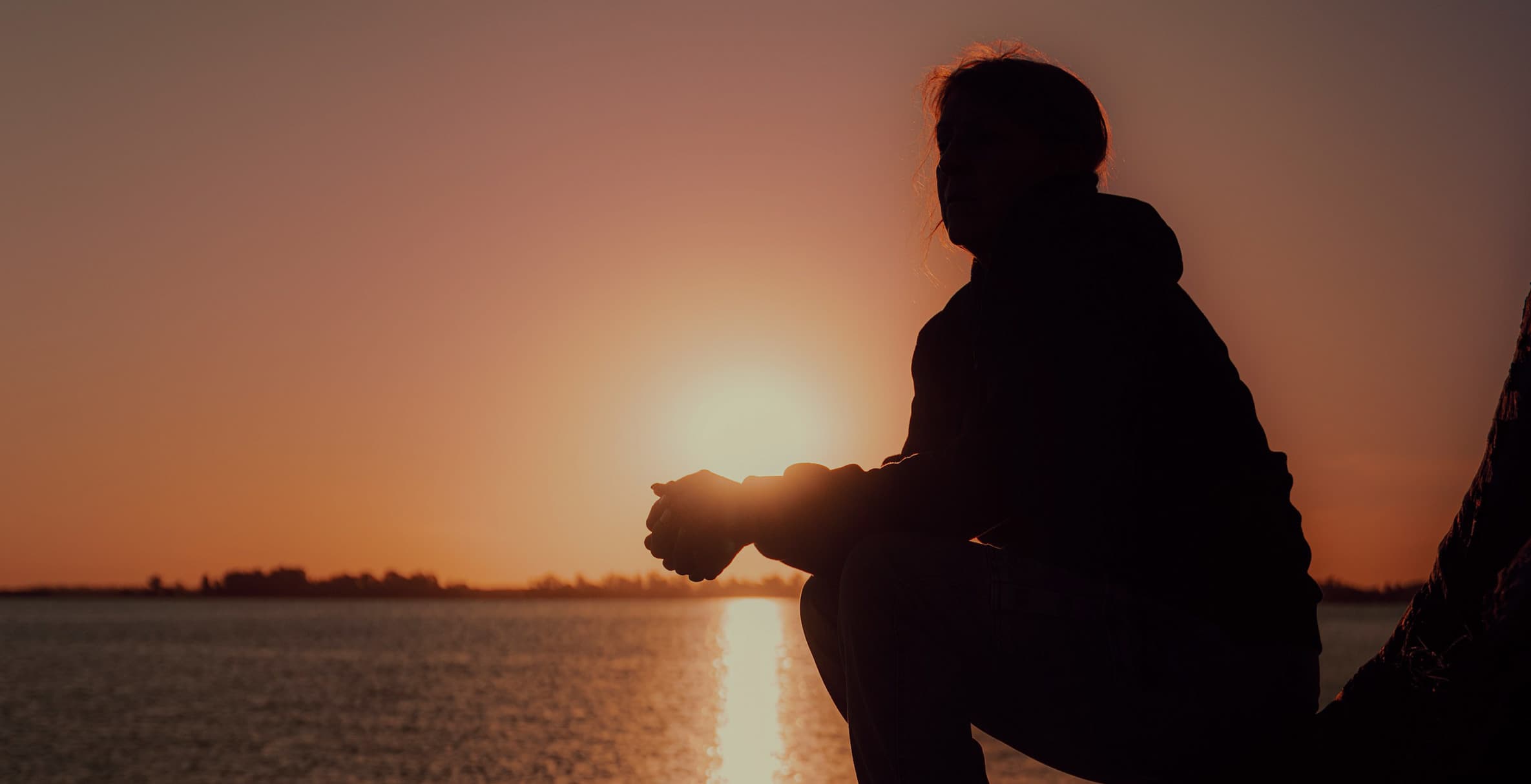 Woman as a silhouette reflecting and looking out to a view of the sunset