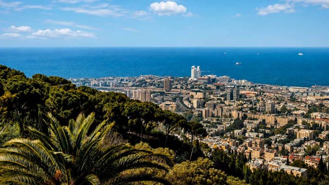 Panoramic view of Haifa, Israel, overlooking the city, Mediterranean Sea, green hills, palm trees, and coastal skyline.