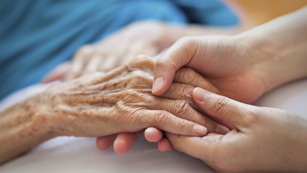 Woman holding elderly woman's hand in a hospital